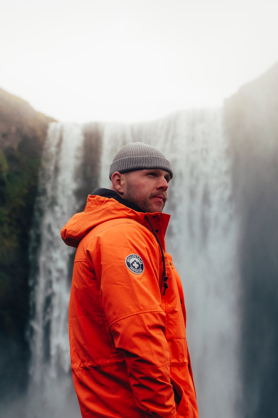 Max Loew in an orange shell jacket before an Icelandic waterfall