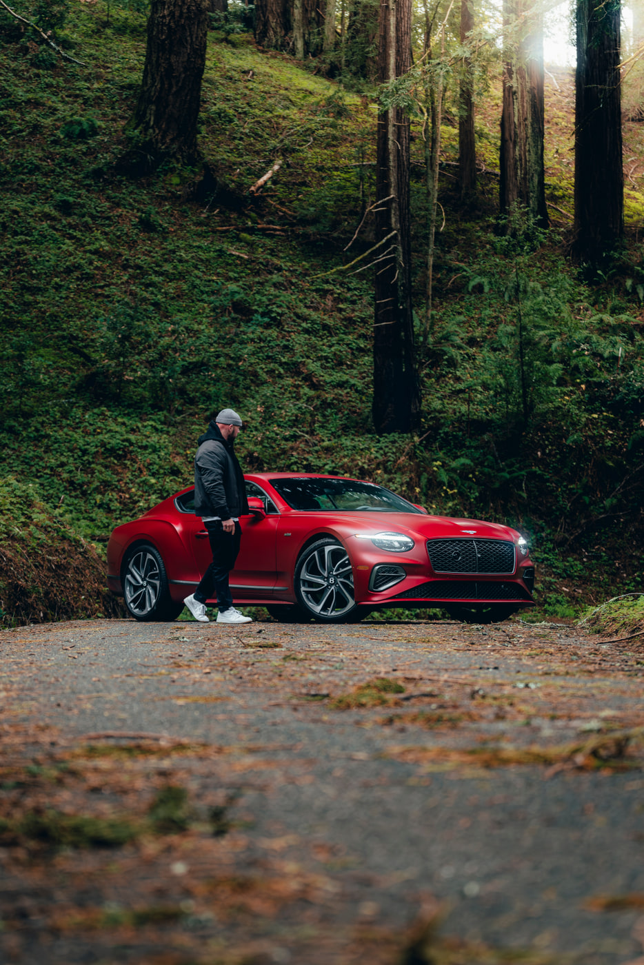 Max beside a red Bentley Continental GT on a redwood road