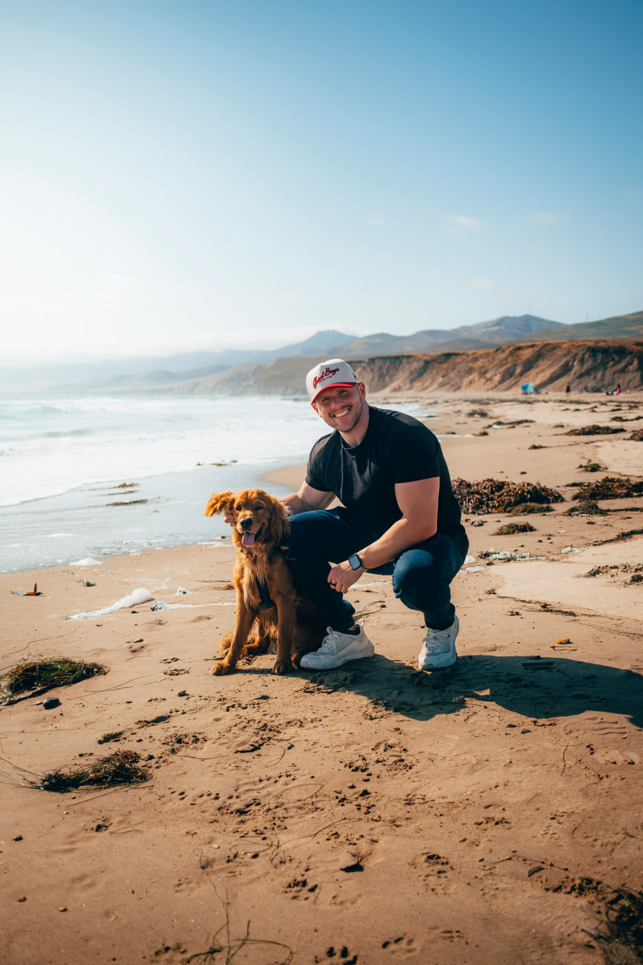 Max kneeling with his golden retriever on a California beach