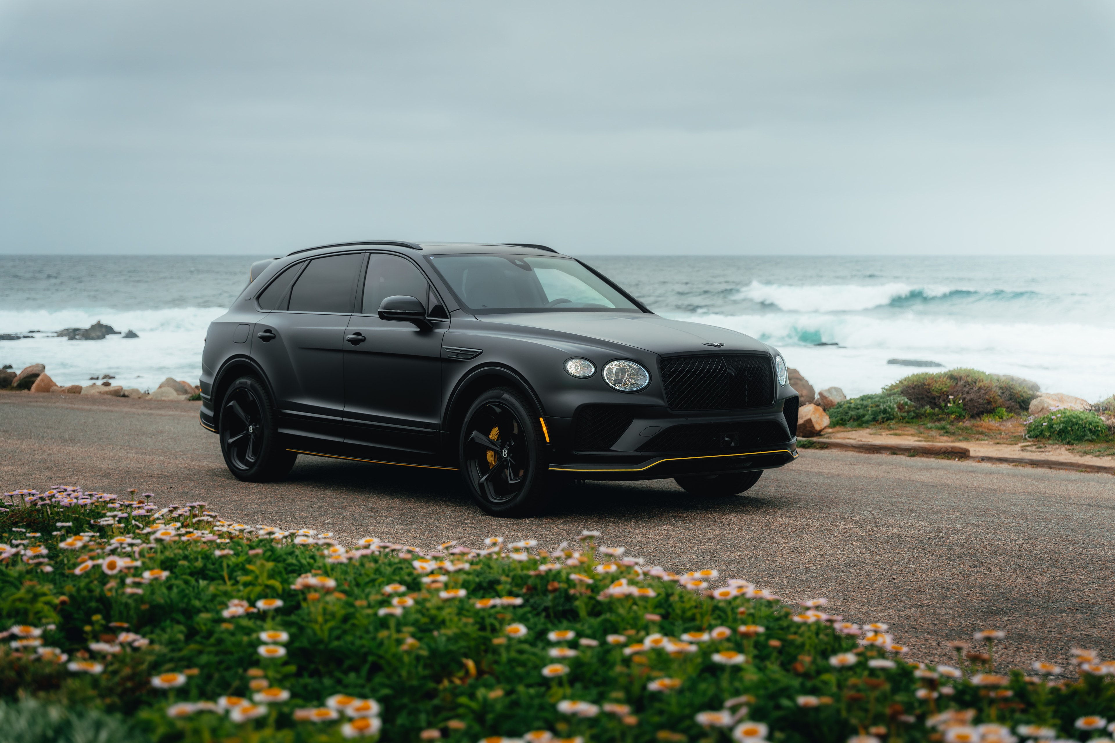 Bentayga front three-quarter with crashing Pacific waves and daisies