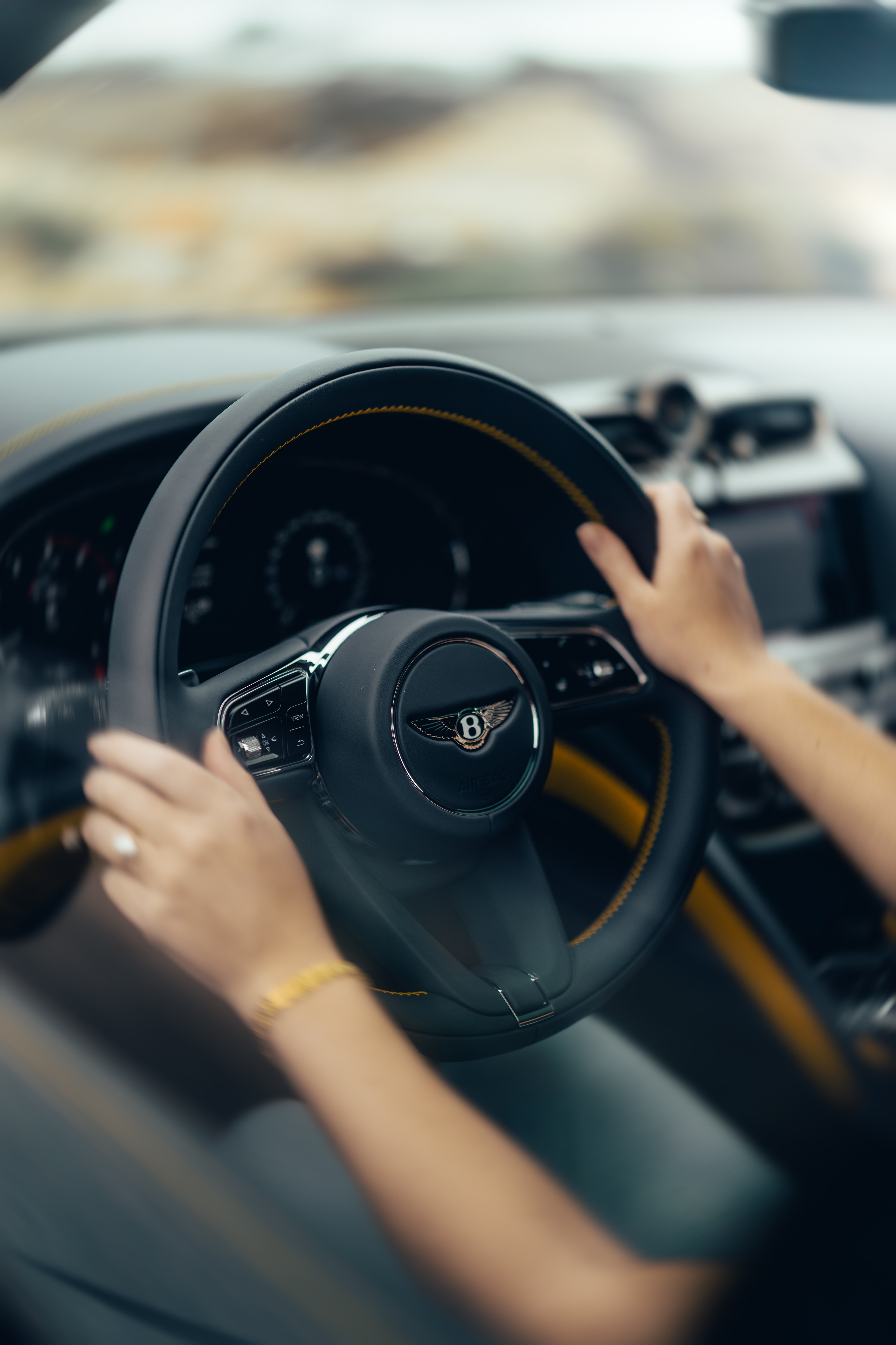 Hands on the Bentayga steering wheel, yellow accent stitching