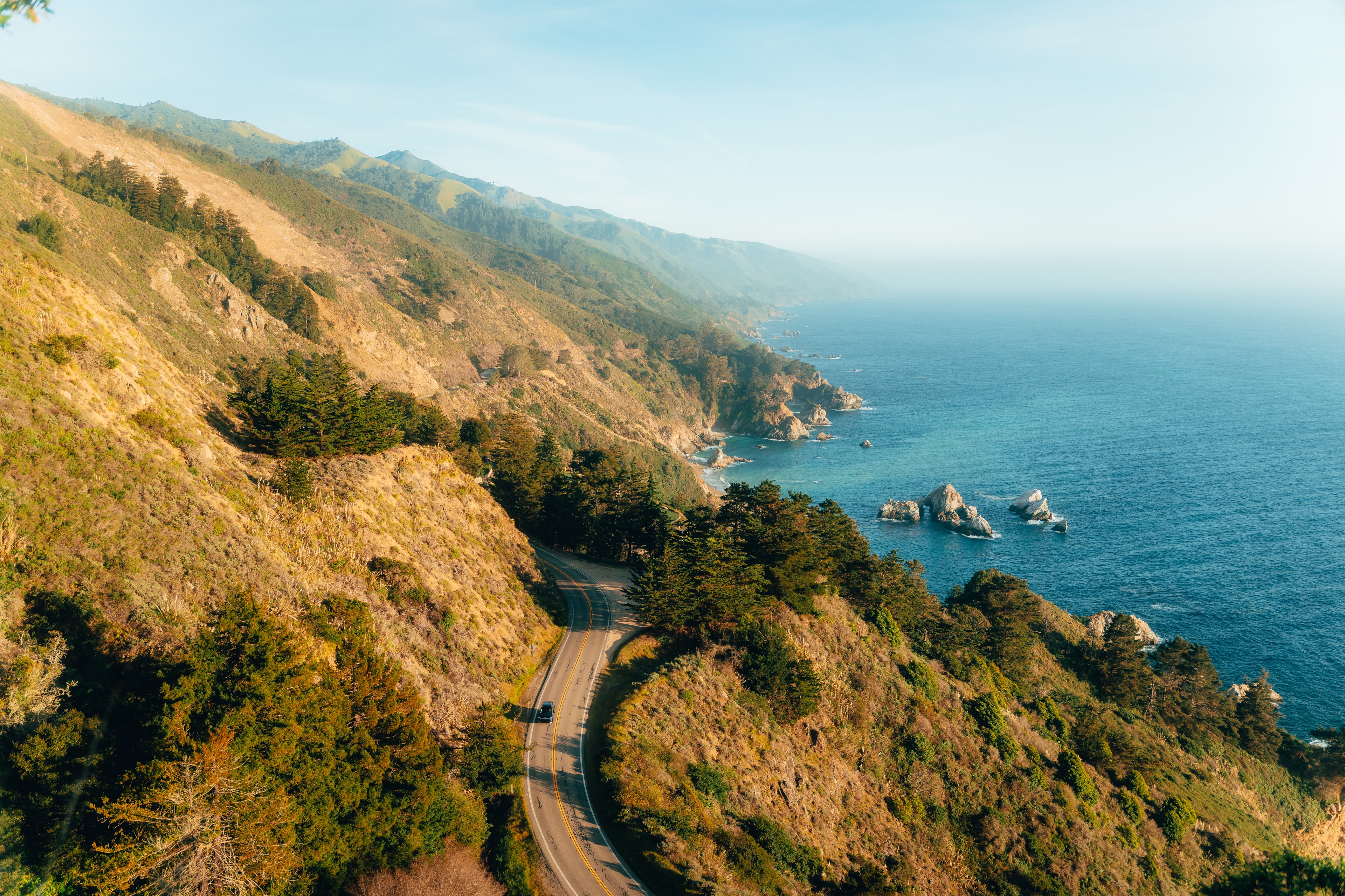 Highway 1 winding along the Big Sur cliffs from above, the IONIQ 9 on the road