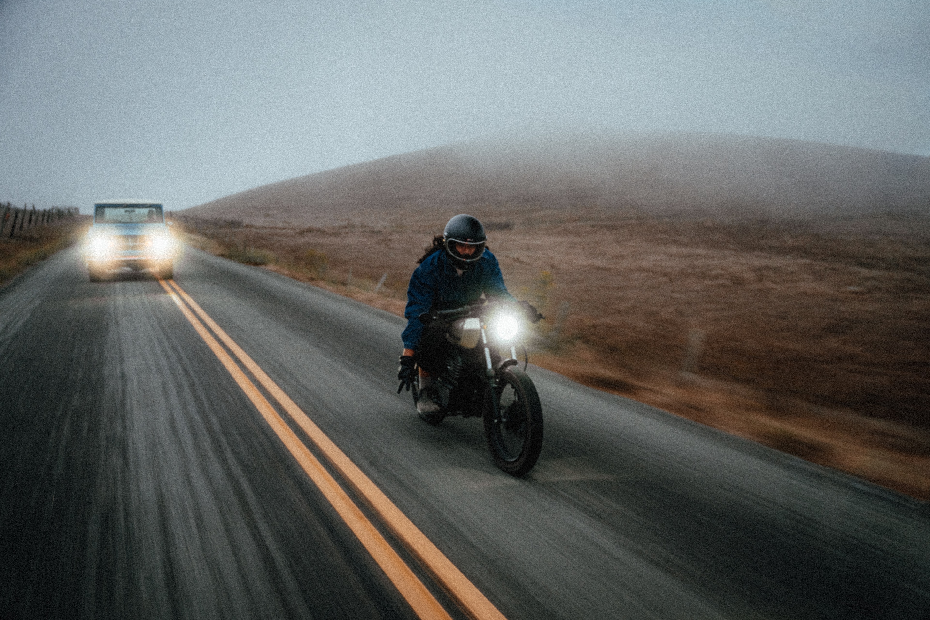 Rider on the Beachman with the blue Bronco behind on a foggy coastal hill, in motion