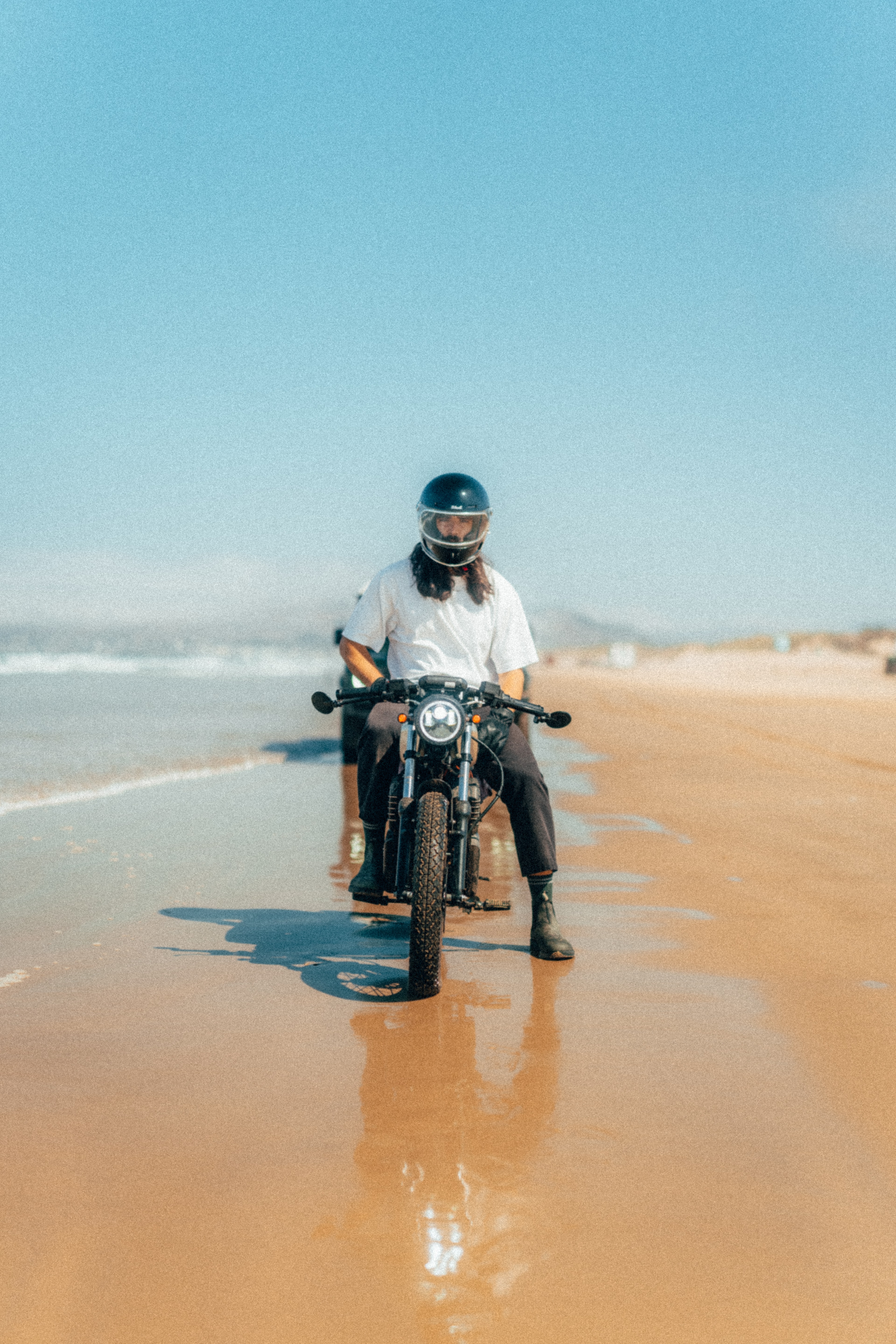 Rider on the Beachman head-on on the sunny beach, reflected in the wet sand