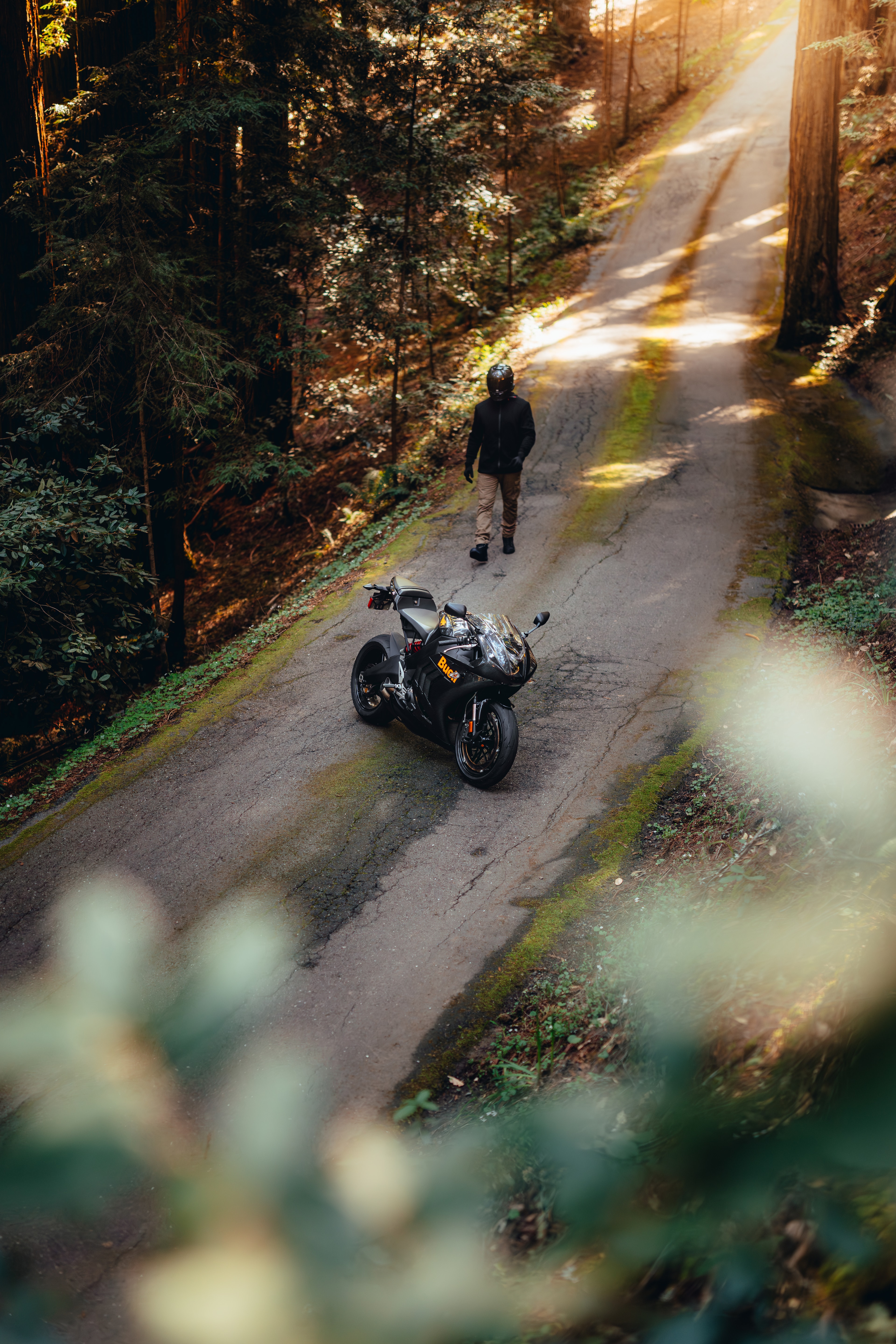 High-angle view of the rider walking up to the Buell on a redwood road