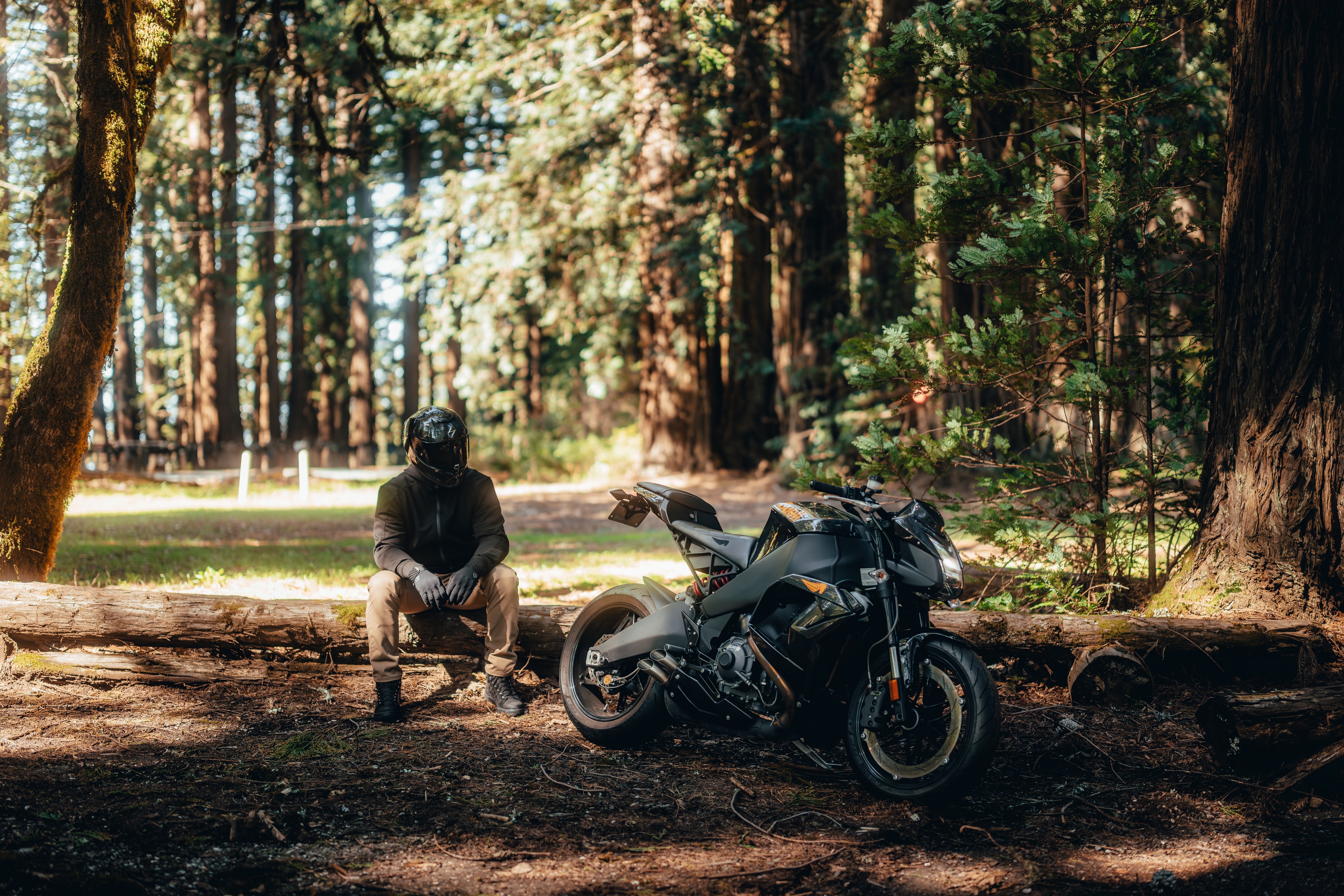 Rider resting on a log beside the Buell in a redwood clearing