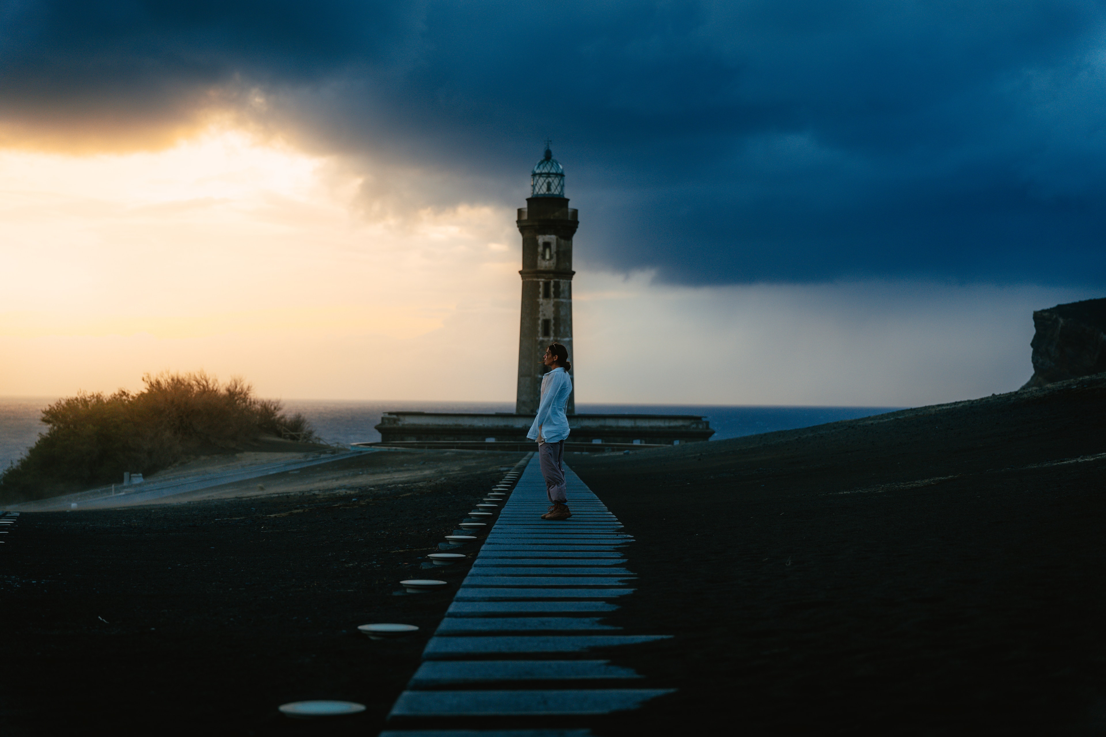 A lighthouse and its breakwater glowing under a moody Atlantic sunset