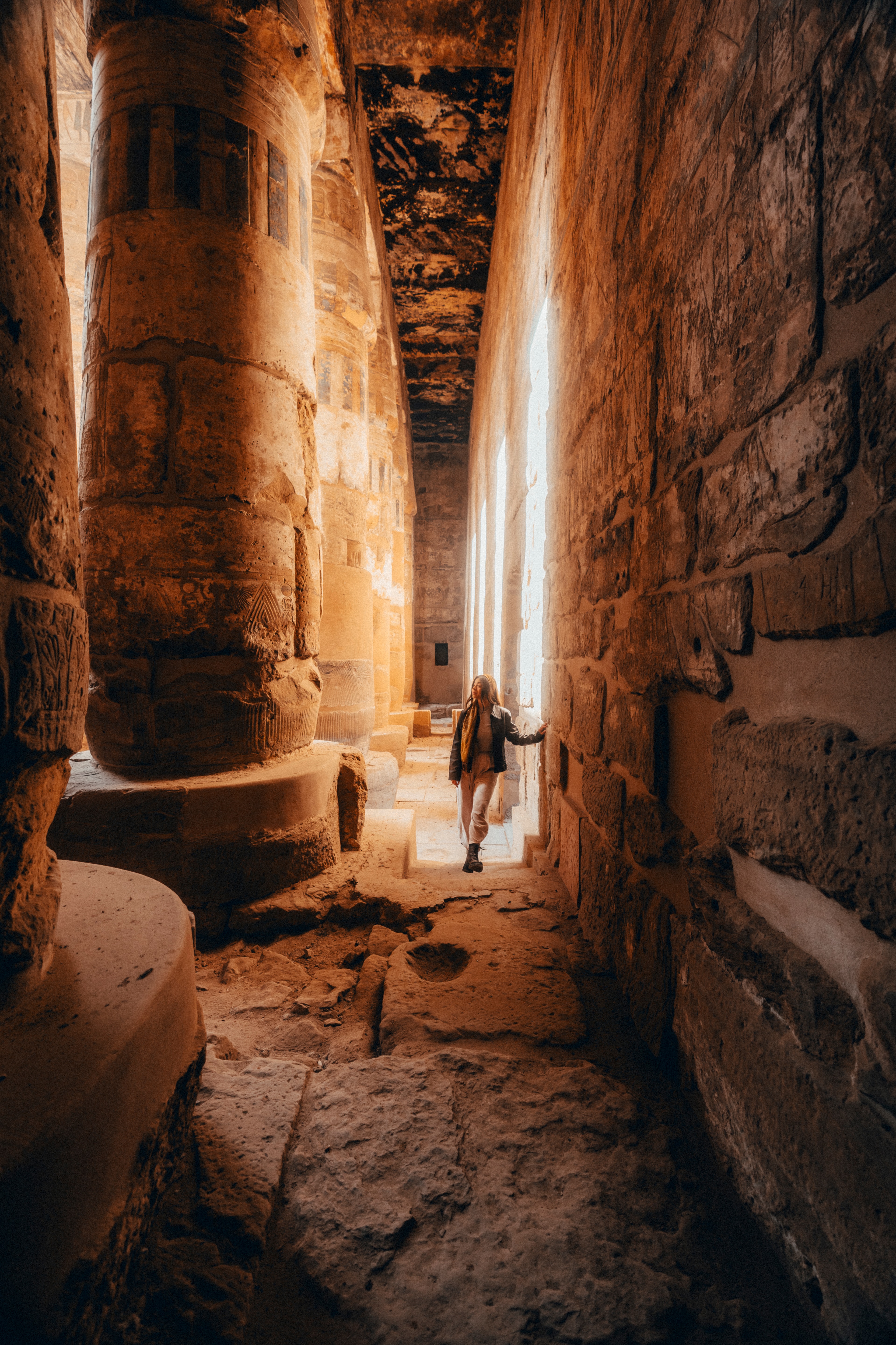 A figure walking down a narrow stone corridor lit by a single shaft of light from above